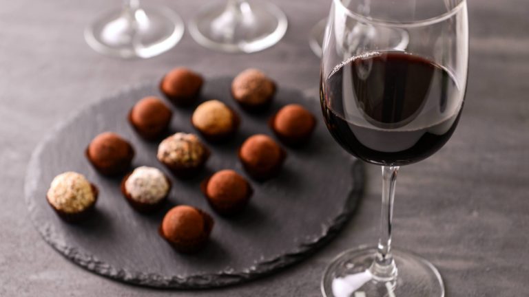Assortment of chocolate truffles beside a glass of red wine