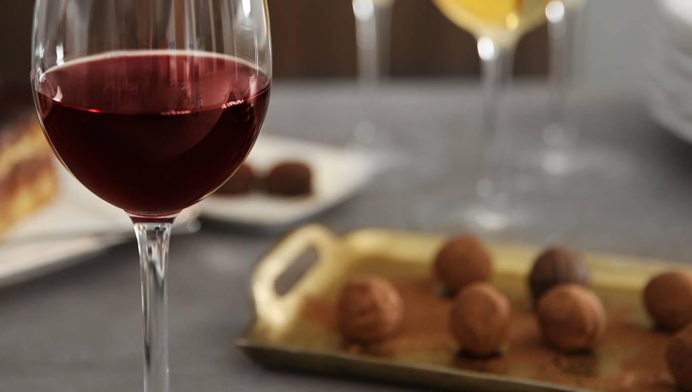 Glass of red wine next to a tray of chocolates and glasses of white wine in the background