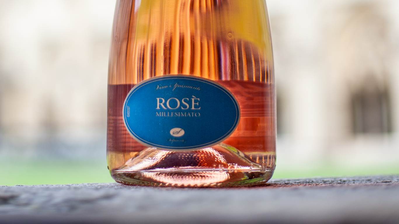 Close up of a bottle of sparkling rose wine in front of a grand building