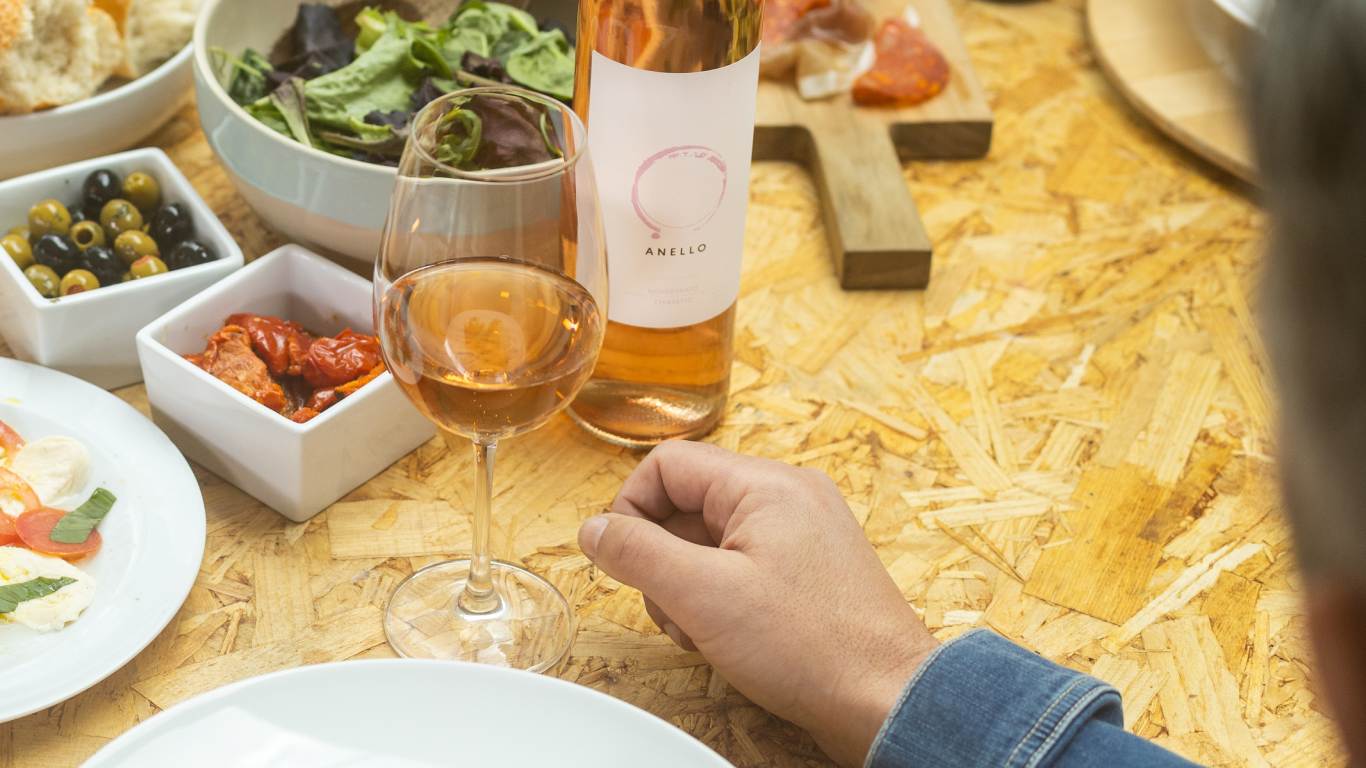 Man sat at a table with plates of food and a bottle and poured glass of rose wine