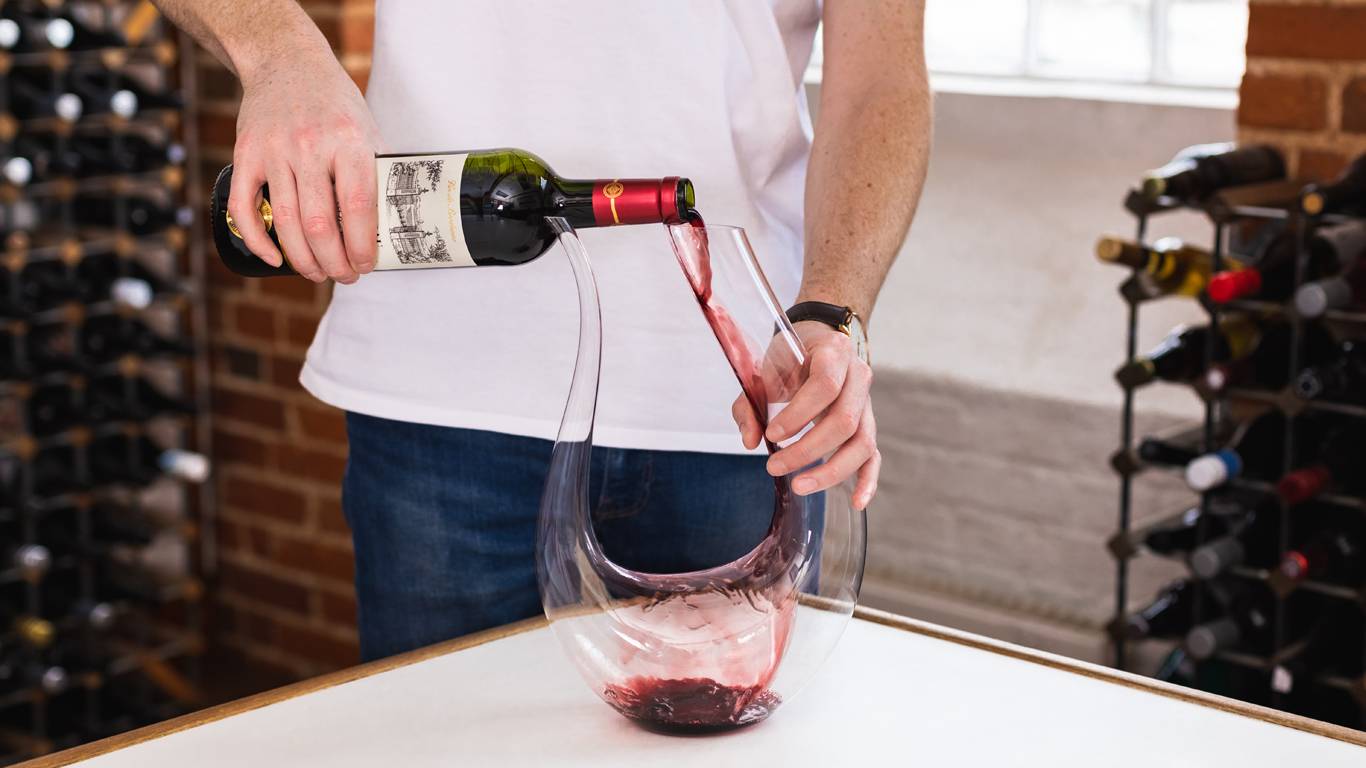 Man beginning to decant a bottle of red wine into a wine decanter
