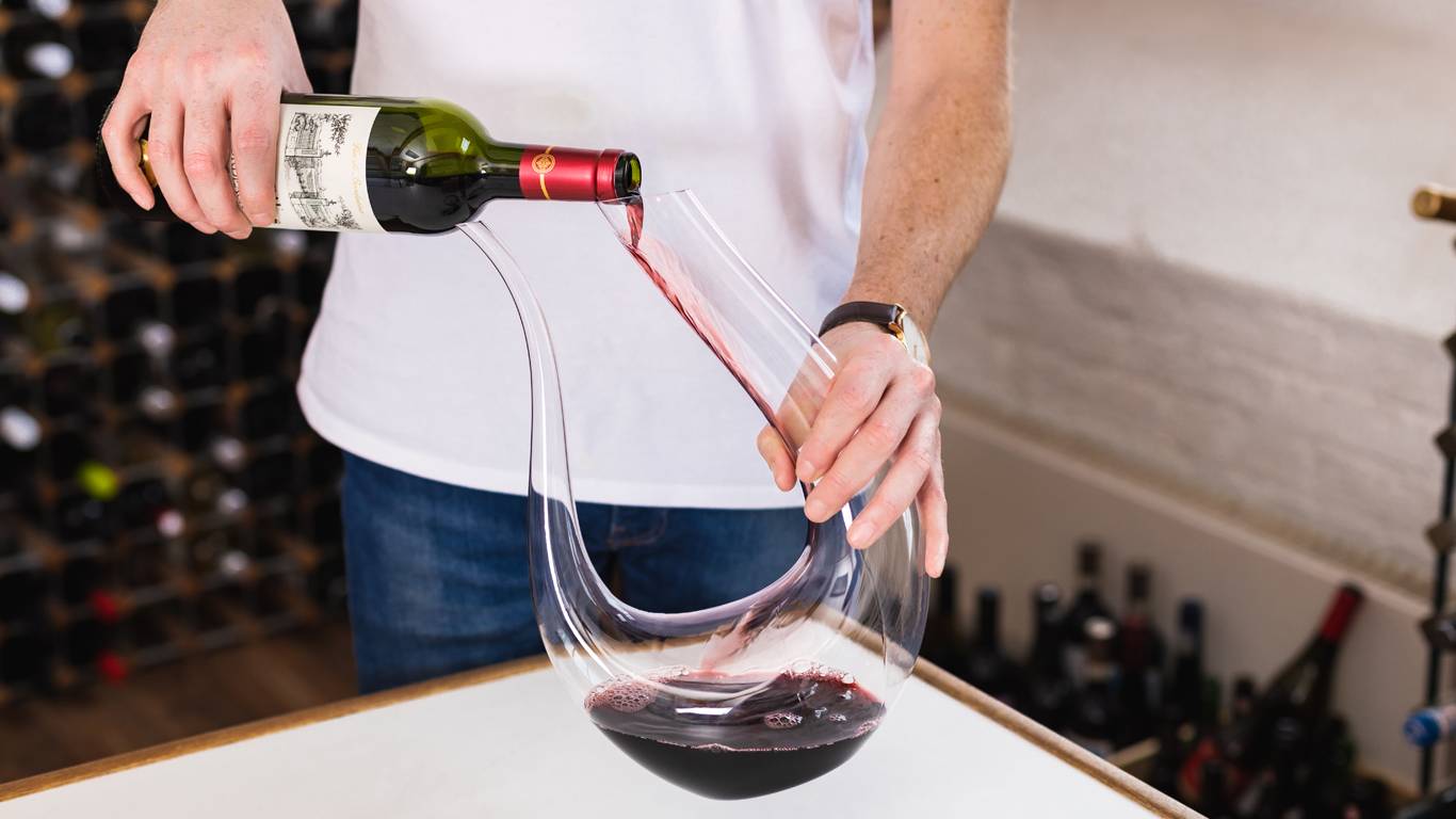 Man in the middle of pouring a bottle of red wine into a wine decanter