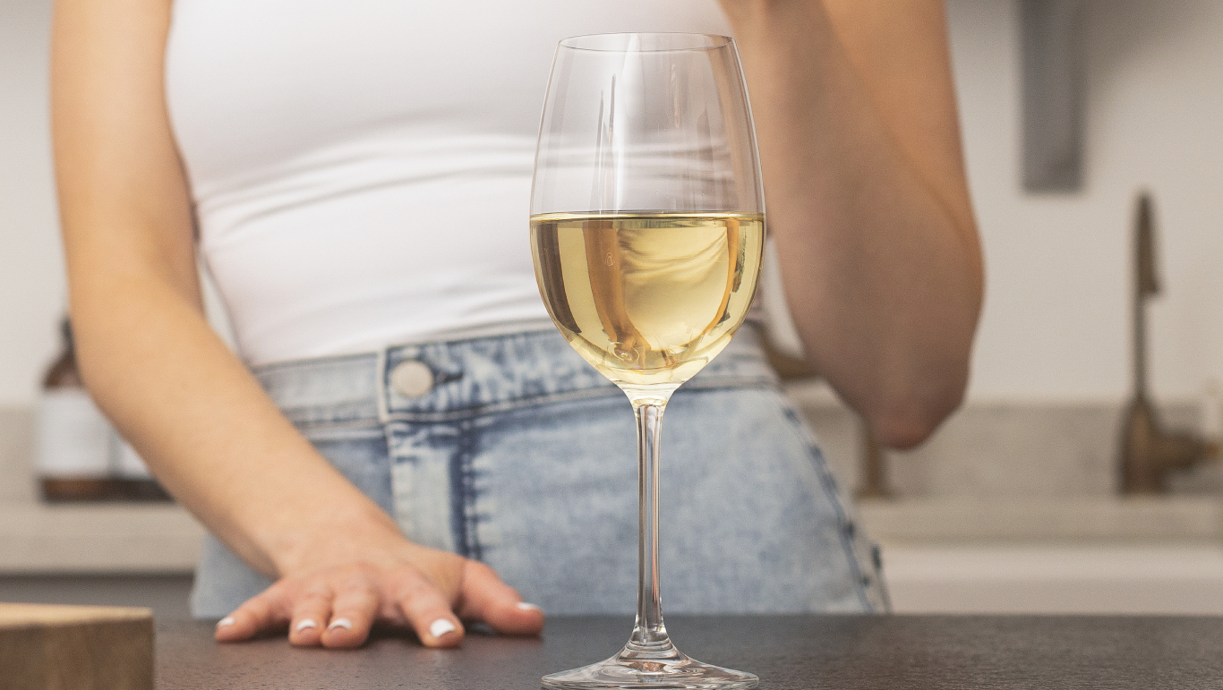 A glass of white wine on a kitchen worktop with a woman in the background