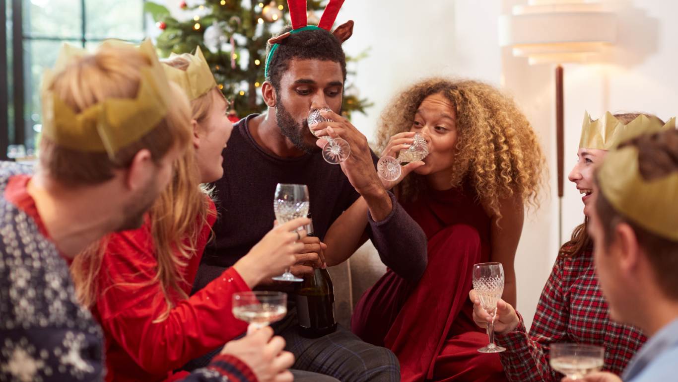Group of friends laughing and drinking sparkling wine on the floor in front of a Christmas tree