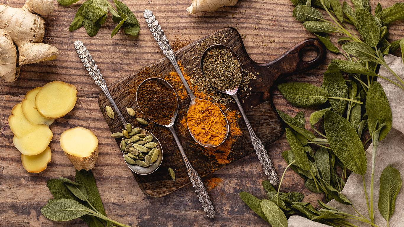 Various pungent herbs on a wooden board including tumeric and ginger