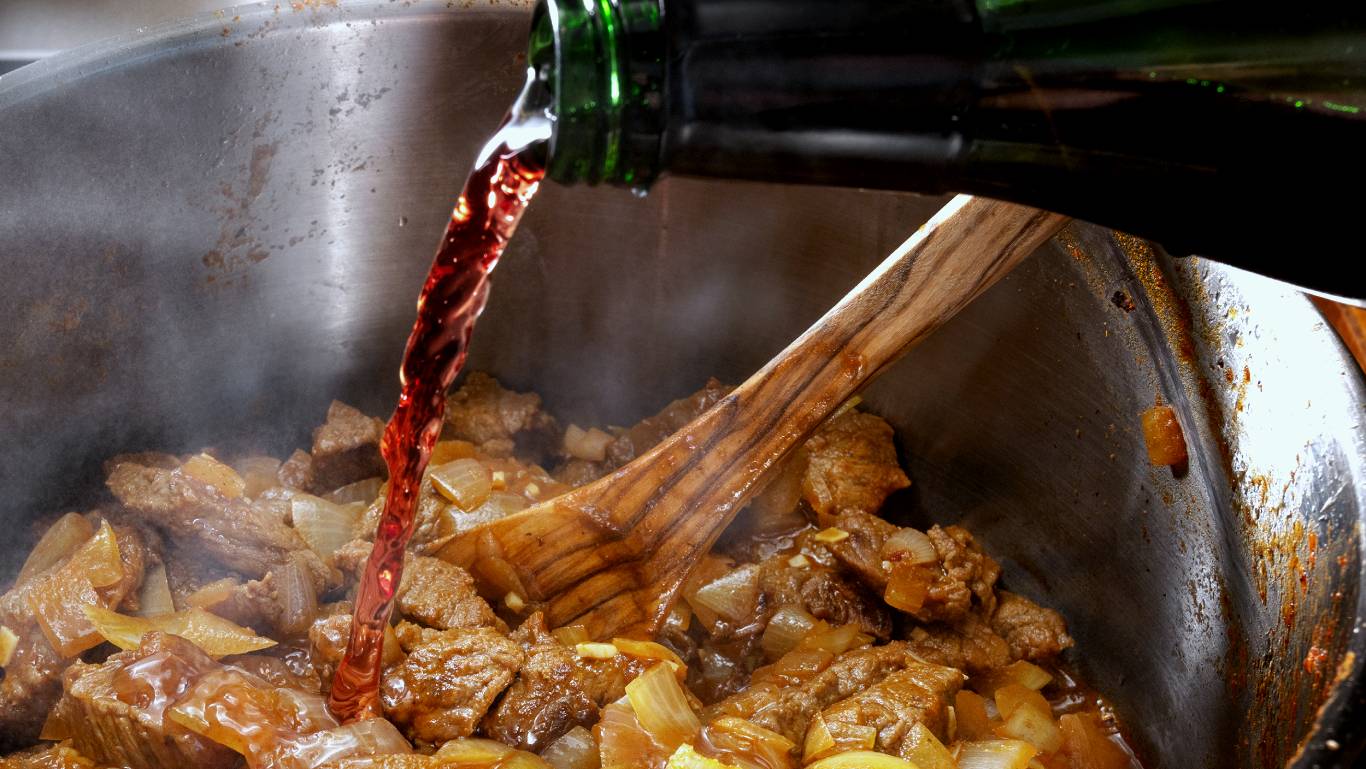 Red wine being poured into food cooking in saucepan
