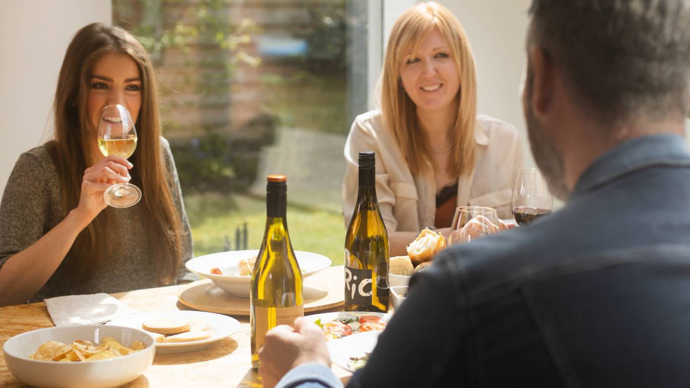Two women and a man sat at a dining table drinking wine and deep in conversation