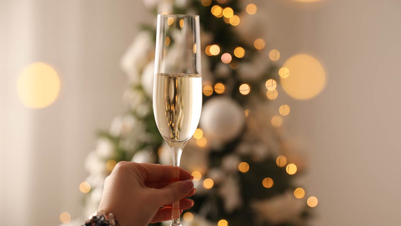 Woman holding a glass of Champagne in front of a lit up Christmas