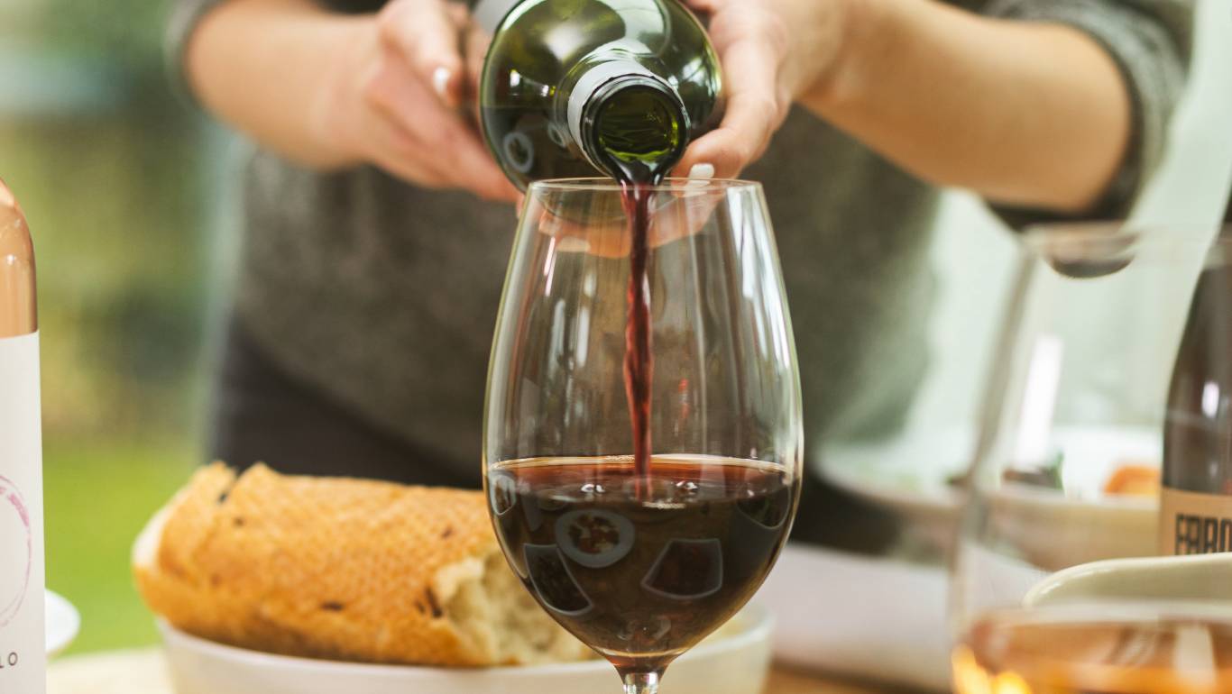 Woman pouring red wine from the bottle into a large wine glass on a dining table
