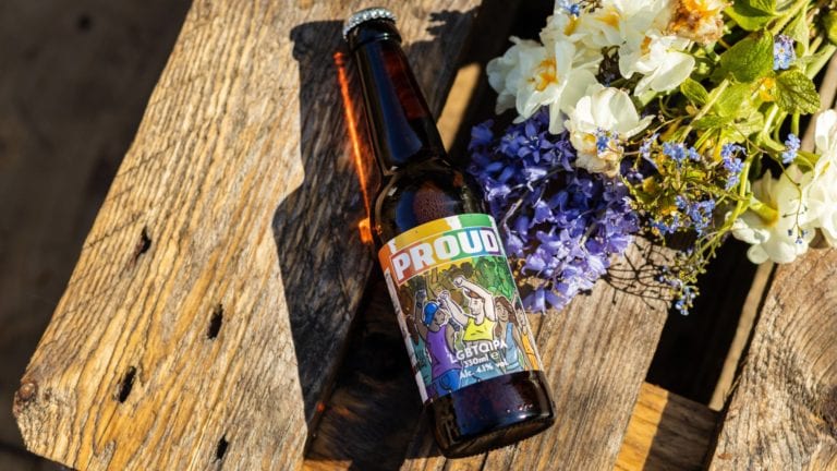 Bottle of PROUD Beer on a wooden garden table beside some flowers in the sunshine