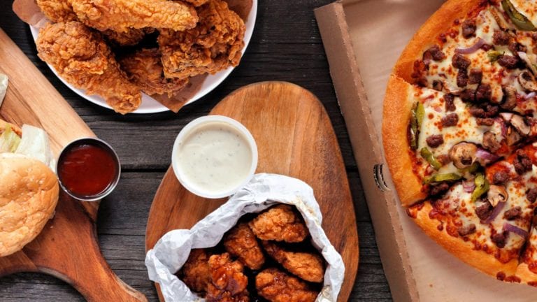 Burgers, fried chicken and pizza laid out on a table on wooden boards with dips