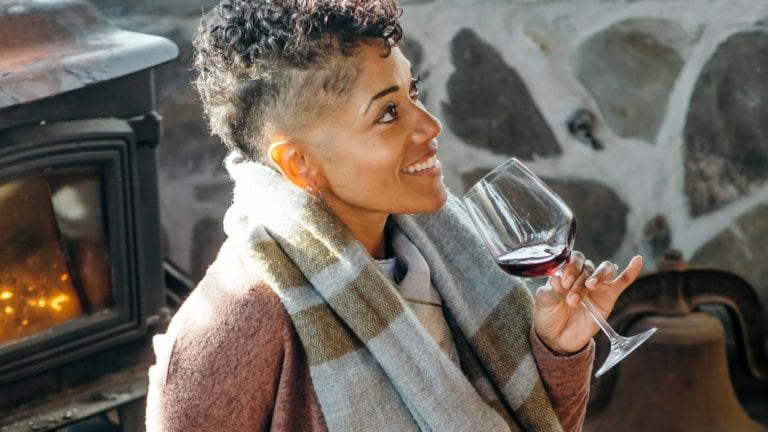 Woman drinking a glass of French red wine by a fireplace