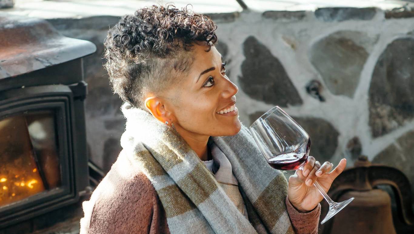 Woman drinking a glass of French red wine by a fireplace looking happy