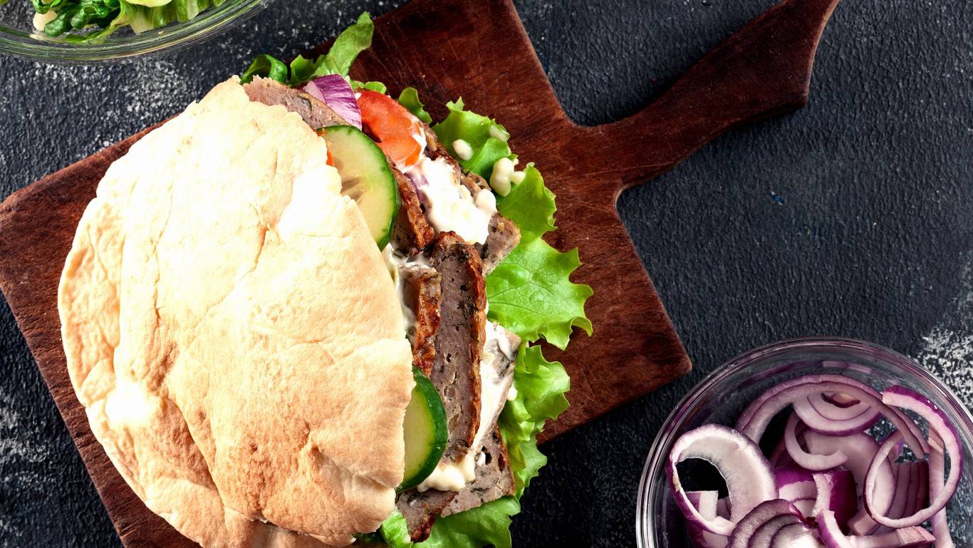 Doner kebab on a wooden board with chopped red onions and lettuce