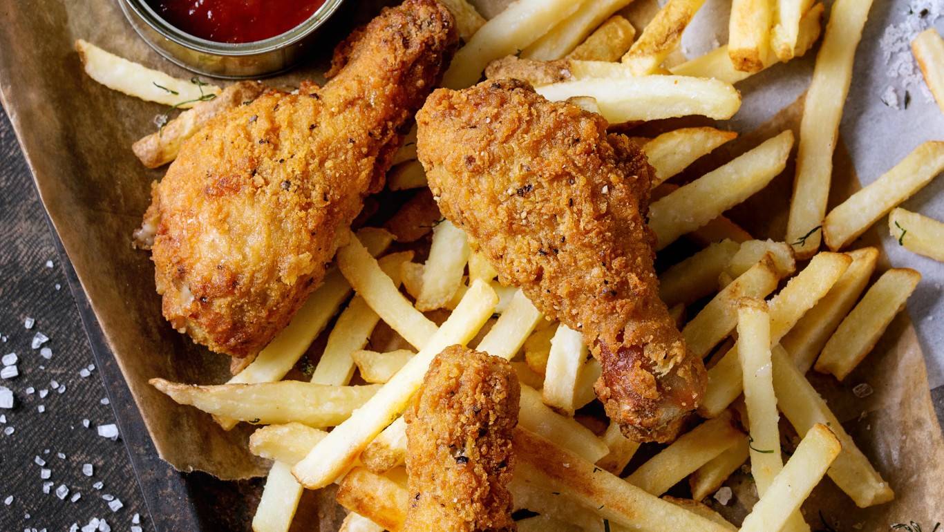 Fried chicken legs and chips on a tray with a pot of ketchup