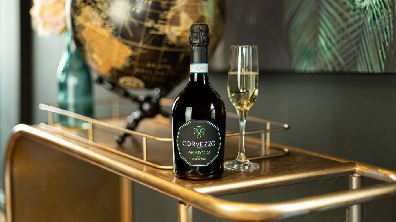 Bottle of Corvezzo Prosecco next to a flute of Prosecco on a gold drinks tray with a globe