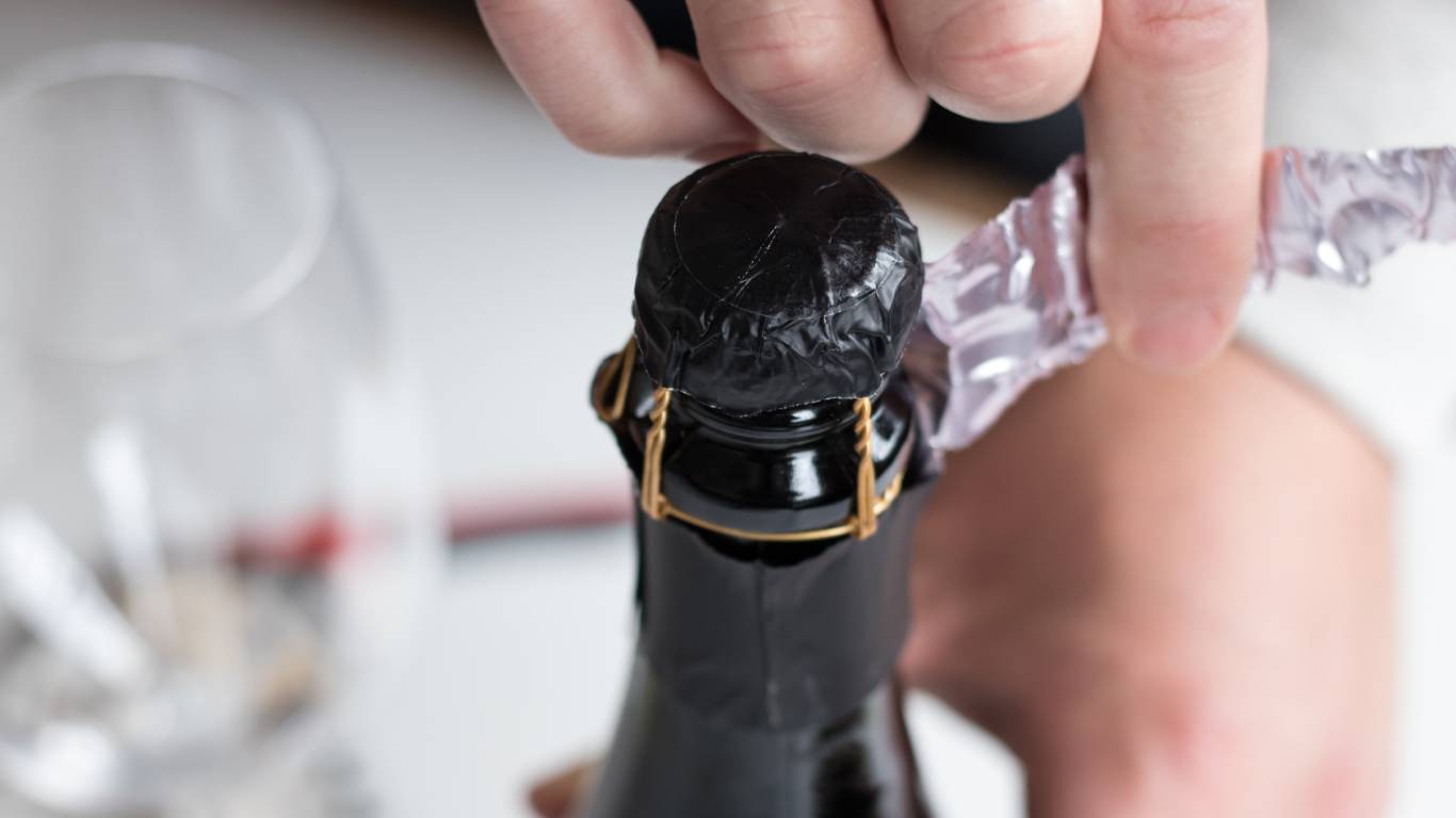 Man unwrapping the foil off the top of a bottle of Prosecco