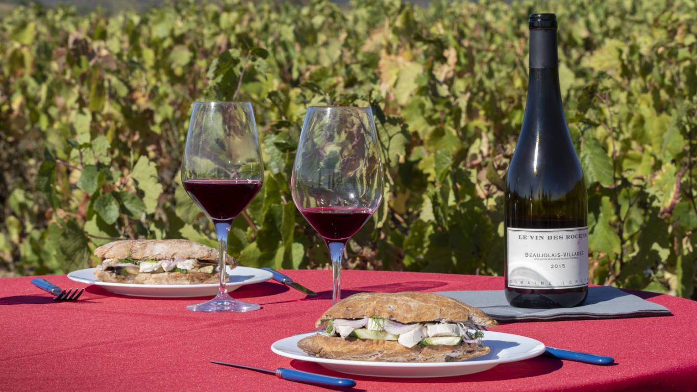 Two glasses of Beaujolais wine on a table in a vineyard by plates of food