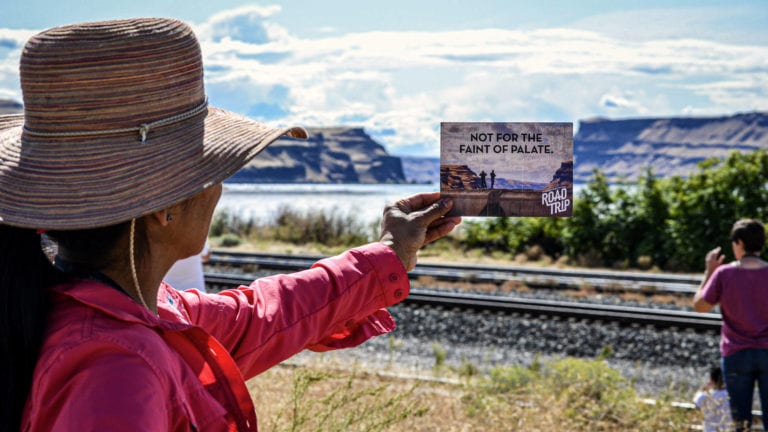 Woman in Washington holding up a postcard about wine against the landscape