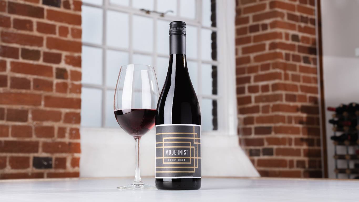 Bottle of Modernist Pinot Noir 2020 with a glass of red wine on a table in front of a window