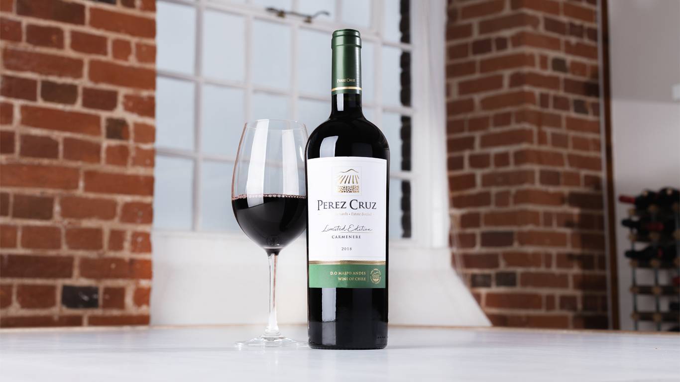 Bottle of Perez Cruz Limited Edition Carmenere 2018 with a glass of red wine on a table in front of a window
