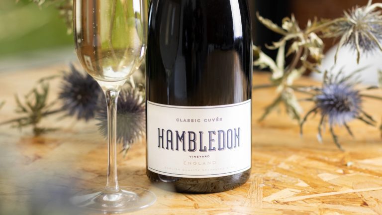 Close up of Hambledon sparkling wine that's available at Virgin Wines, beside a Champagne flute of sparkling wine and flowers