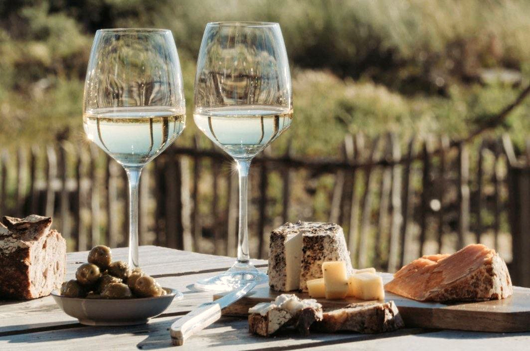 Two glasses of white wine with plates of cheese and bread outside by beach