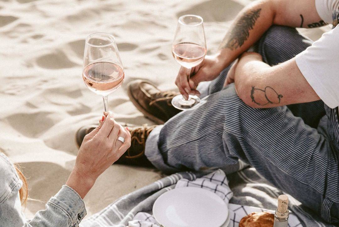 Two people drinking glasses of rose wine in the beach with a picnic