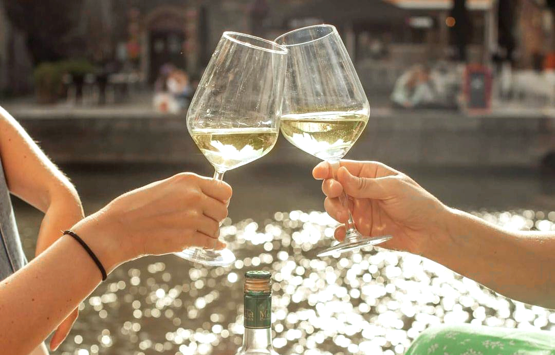 Two people toasting with glasses of white wine in front of Garonne river in the sunshine