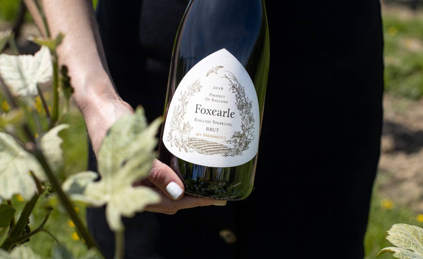Woman holding a bottle of Henners Foxearle English Sparkling Brut 2016 in the sunshine in Henners vineyard