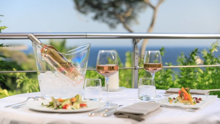 Table setup over looking the sea with a bottle of Provence rosé in an ice bucket with two glasses of rosé wine and two salads