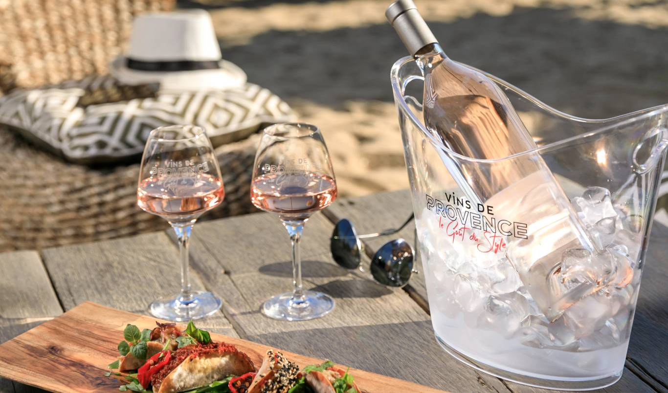 Glasses of Provence rose on a table outside with a plate of food, a sun hat and an ice bucket