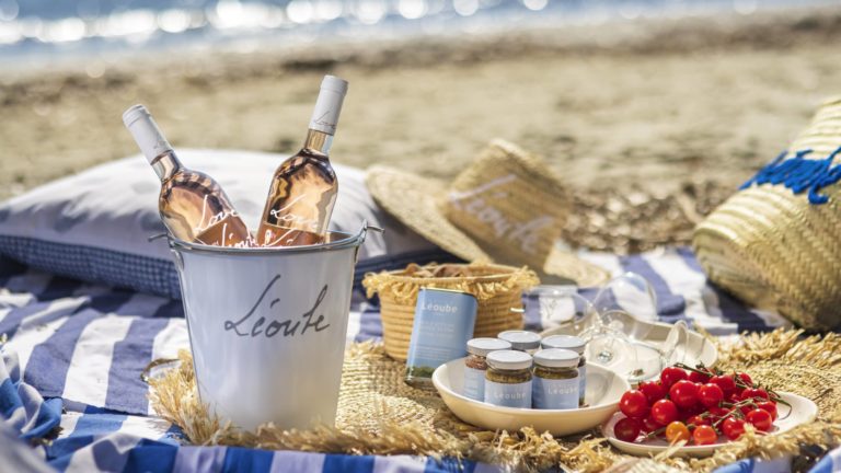 Bottles of sustainable Provence wine by Chateau Leoube in a branded ice bucket with a picnic on a beach