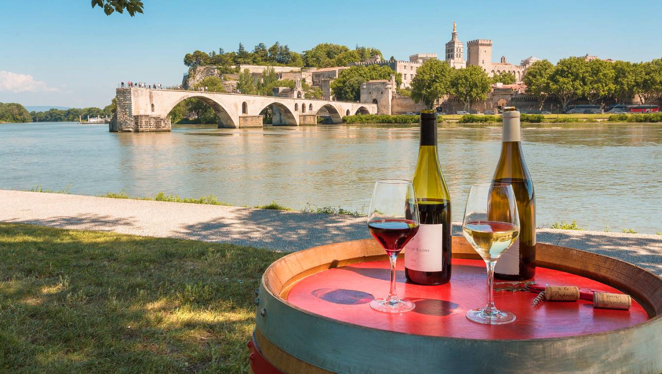 Bottles of wine and two glasses of poured wine on a barrel overlooking the river Rhone in France