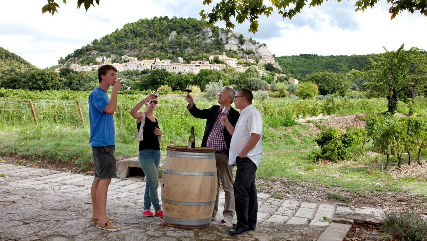 Four people wine tasting around a barrel in a vineyard in Rhone Valley