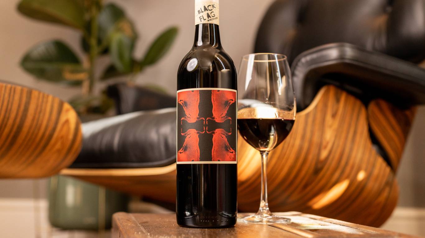 Black Flag Winemakers McLaren Vale Cabernet Sagrantino 2018 by a glass on wine on a coffee table by a chair