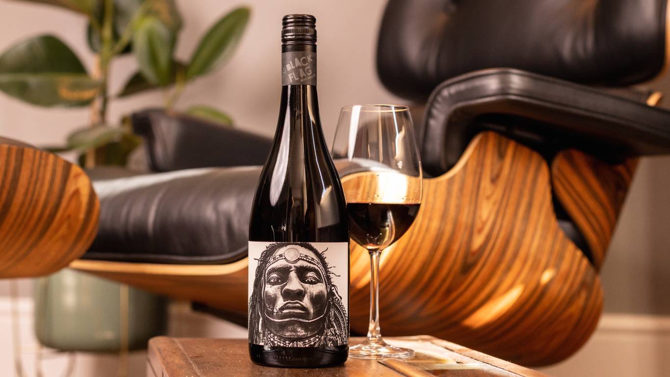 Black Flag Winemakers Old Vine Grenache 2018 by a glass of wine on a coffee table by a chair