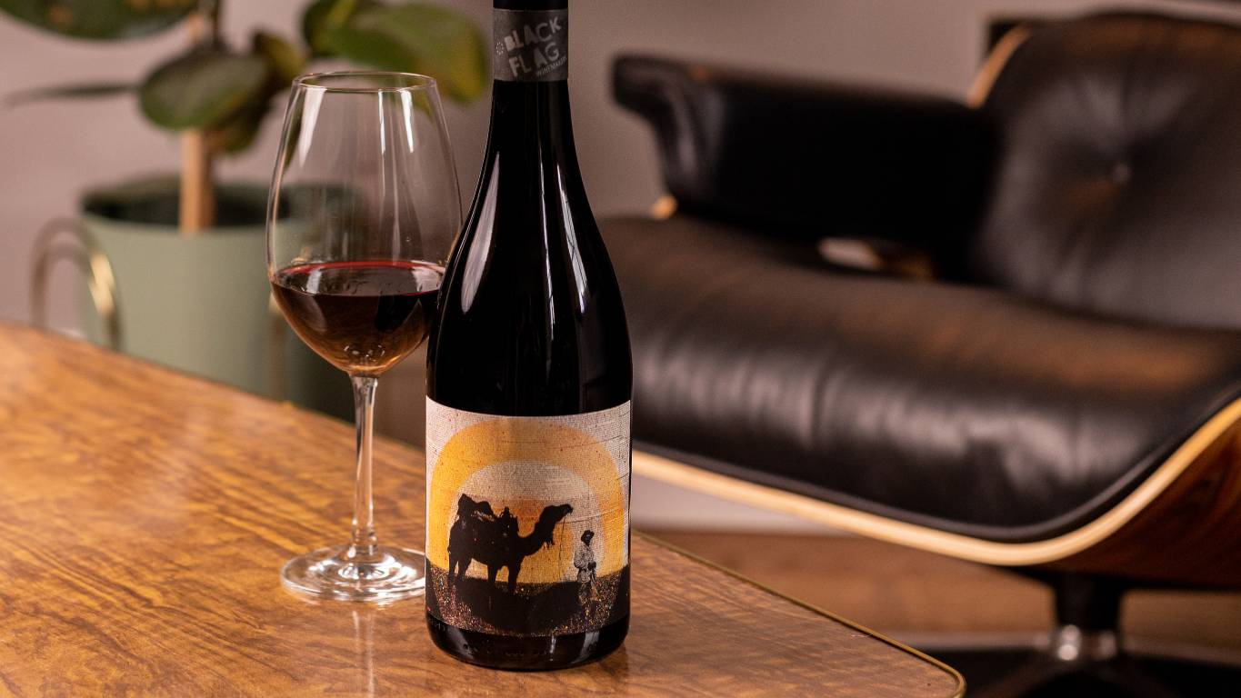 Black Flag Winemakers South Australian Shiraz 2018 by a glass of wine on a coffee table by a chair