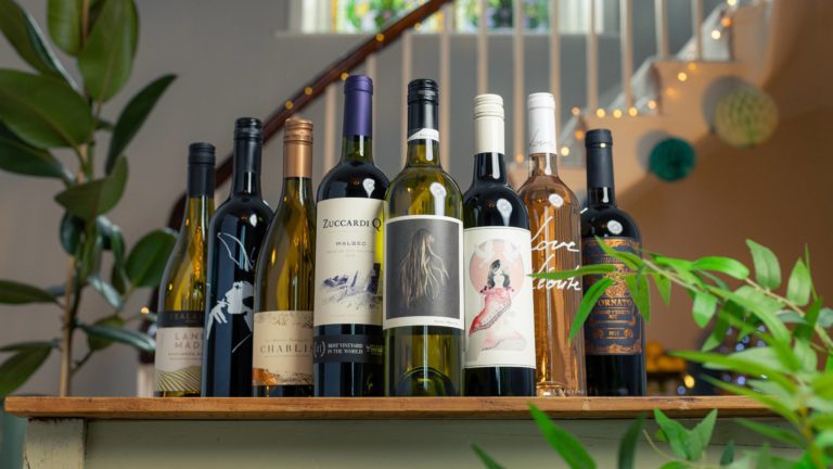 Line-up of vegan wines available at Virgin Wines, on a table in front of a staircase with fairy lights on it