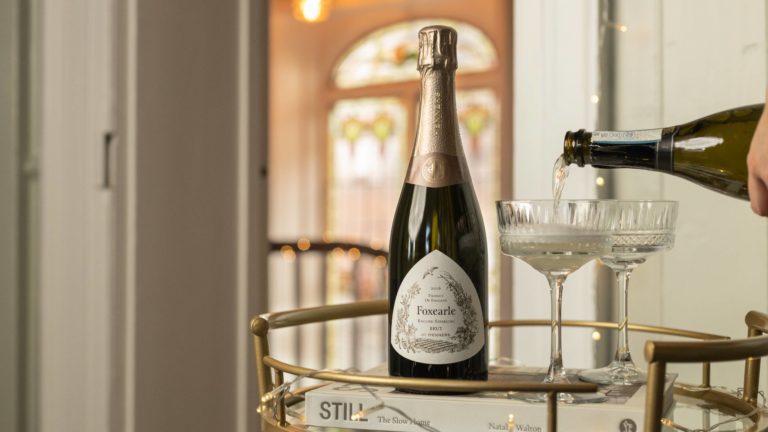 Champagne alternative sparkling wine being poured into a coupe glass on a gold drinks trolley with a bottle of Henners Foxearle English Sparkling Brut 2016 and fairy lights
