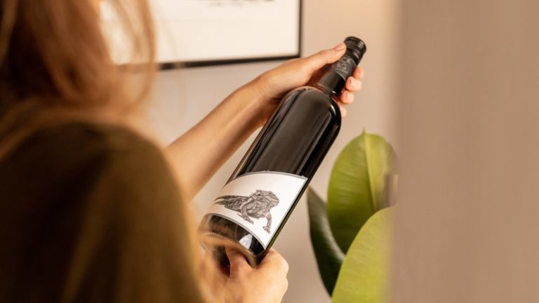 Woman looking at a bottle of Black Flag Winemakers Langhorne Creek Adelaide Hills Shiraz 2018 by a plant