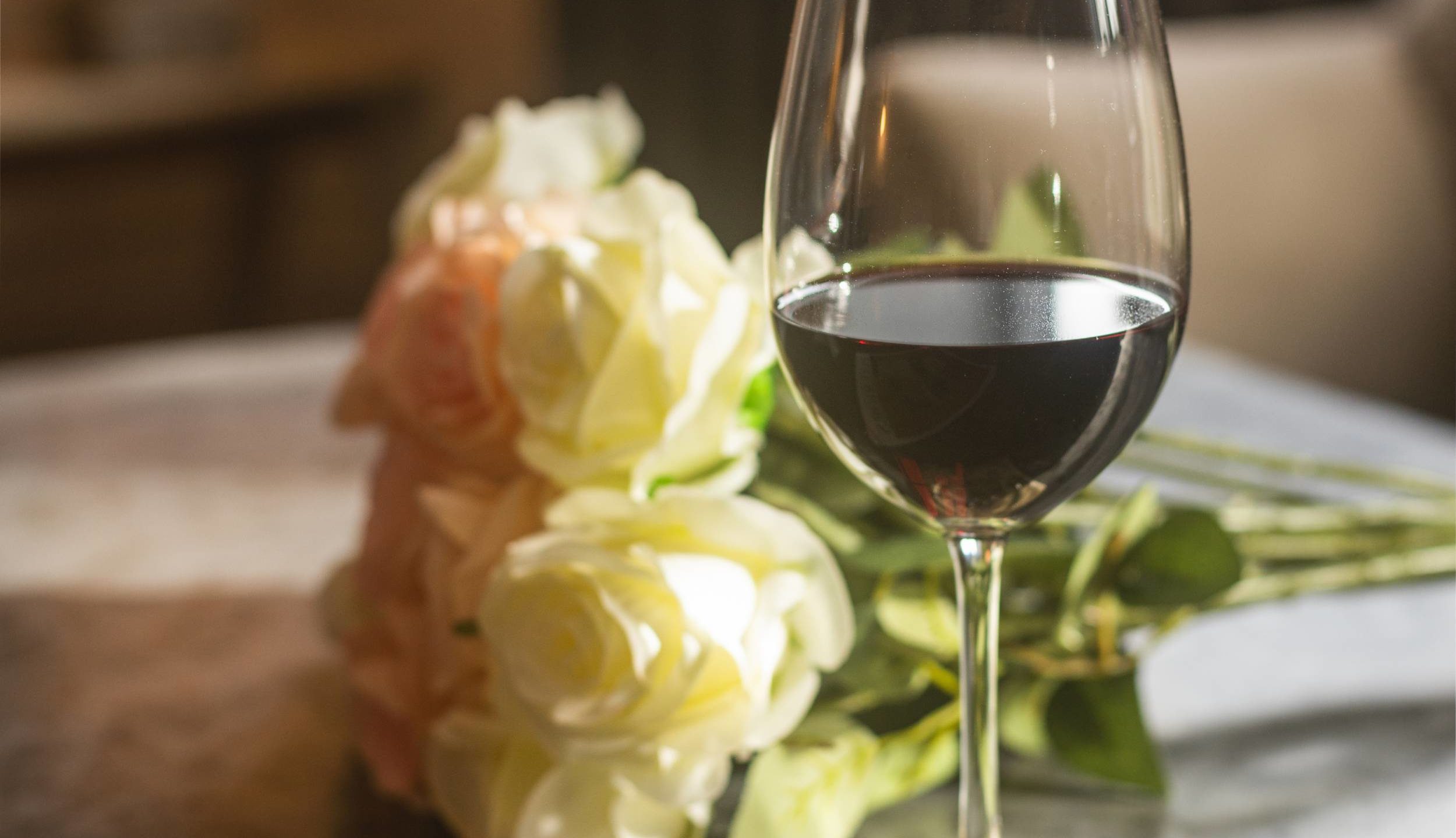 Glass of red wine on a table beside some flowers