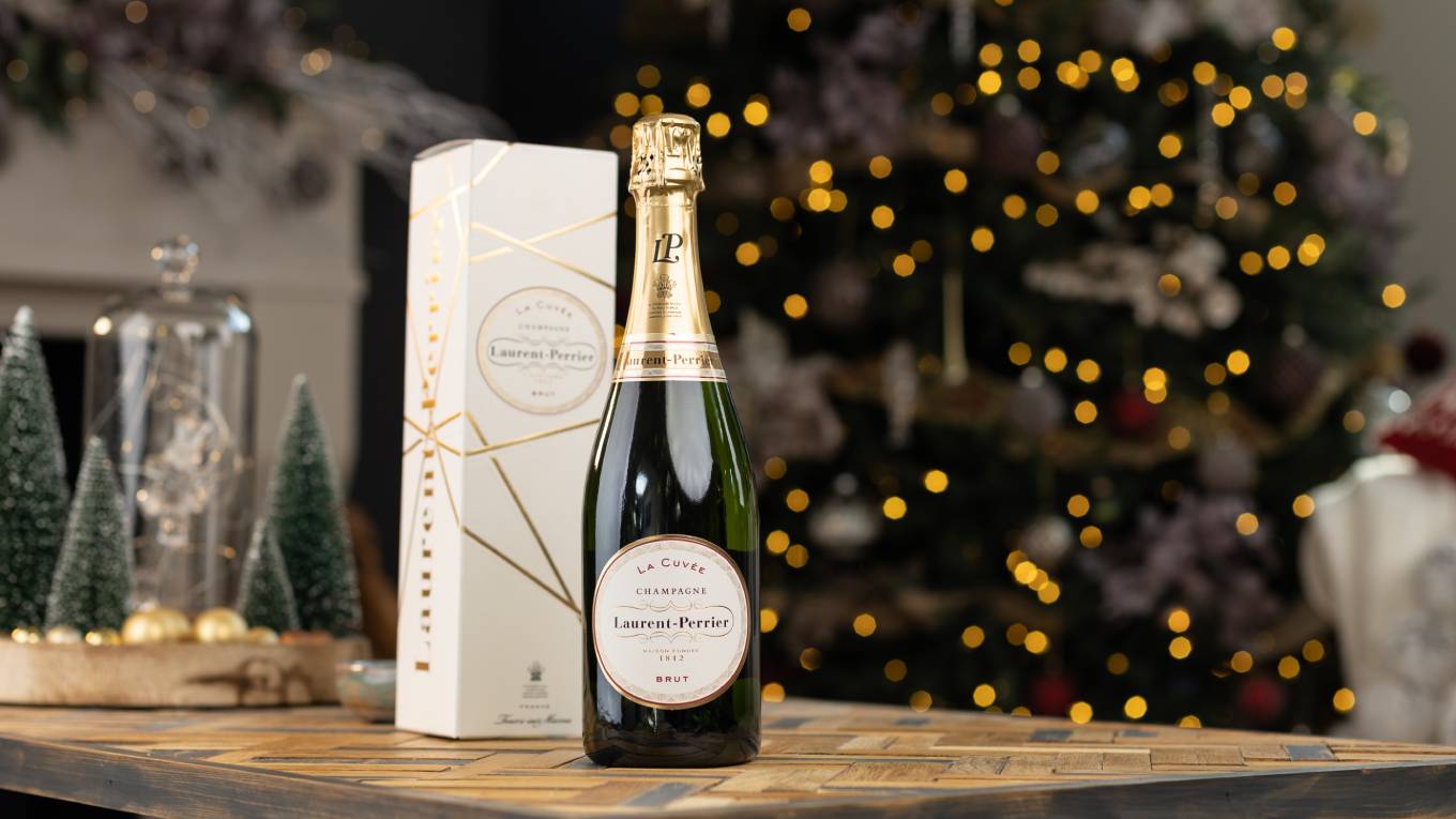 bottle of champagne and gift box on table in front of Christmas tree