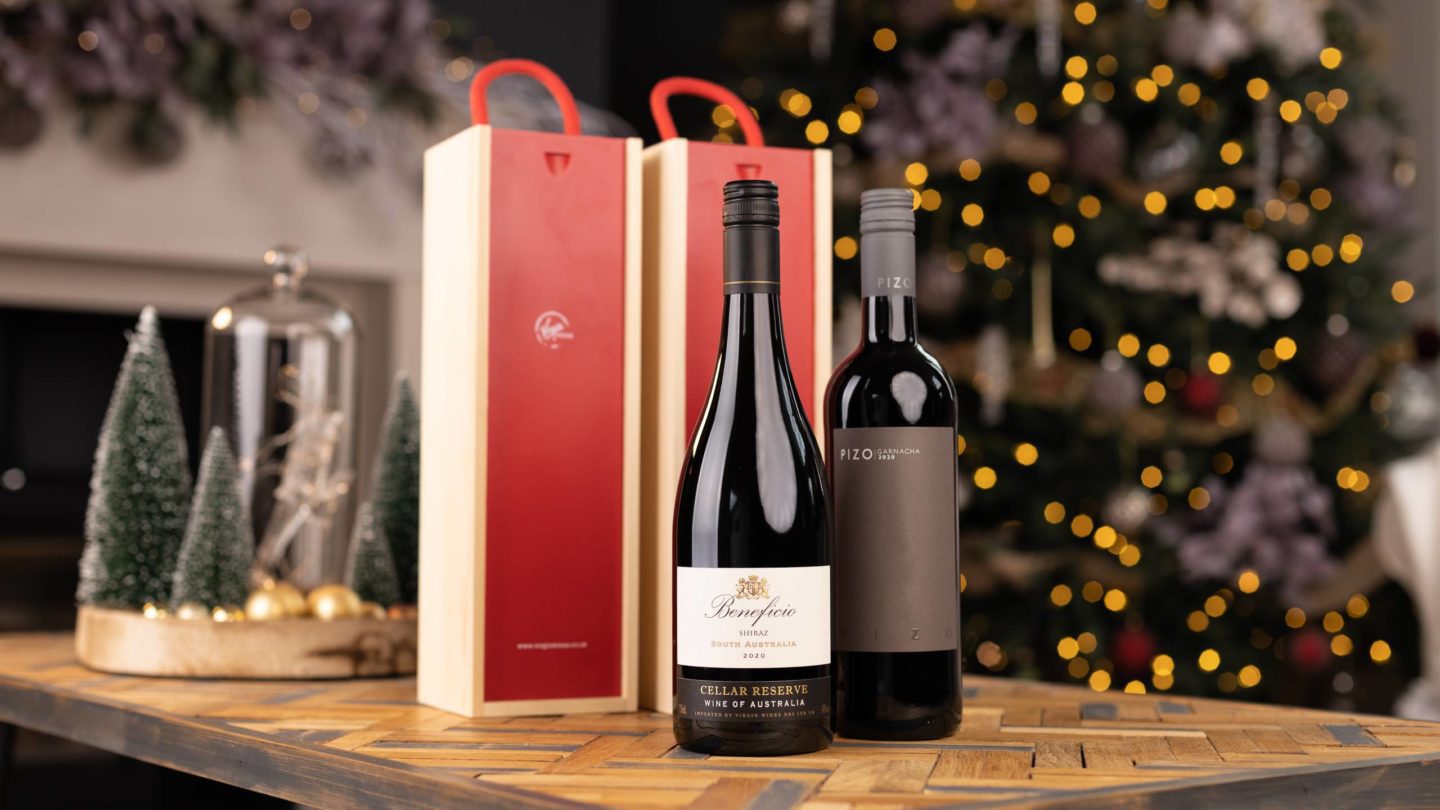 two bottle of wine and two wooden gift boxes on table in front of Christmas tree