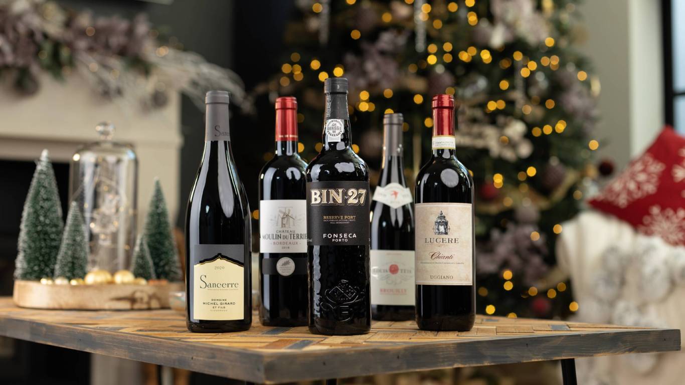 Five red wine bottles on a coffee table in front of a large Christmas tree