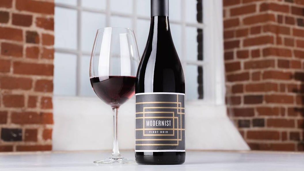 Bottle of Modernist Pinot Noir 2020 with a glass of red wine on a table in front of a window