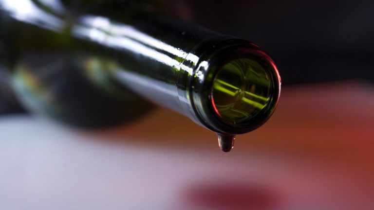 Closeup of red wine bottle on its side with a tiny drop of red wine dropping from the bottle mouth