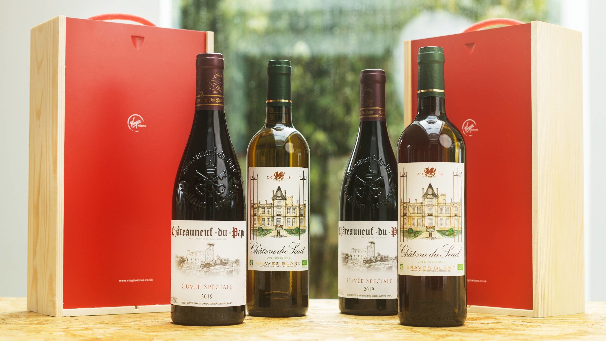 Four bottles of premium French wine on a table with branded Virgin Wines presentation boxes