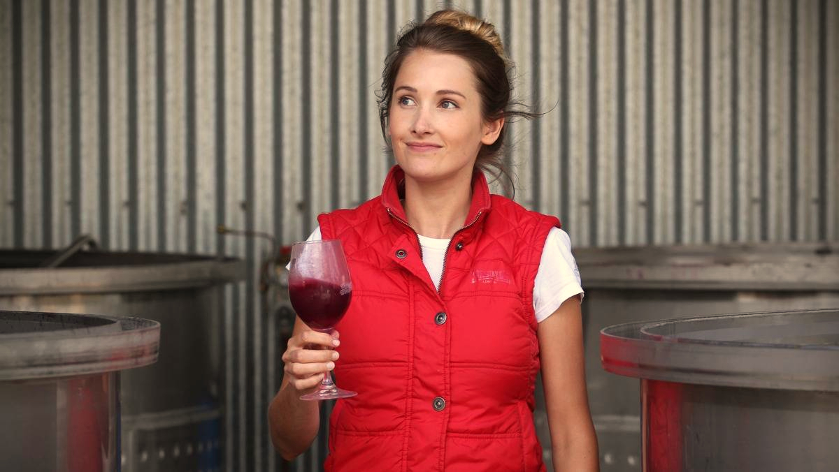 One of our women in wine, Jess Hardy of Loom Wine, holding a glass of grape juice next to some tanks in the winery