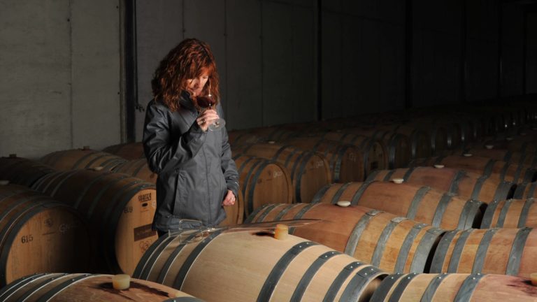 Female winemaker Rosalia Molina of AltoLandon Winery sniffing a glass of red wine in a winery full of barrels